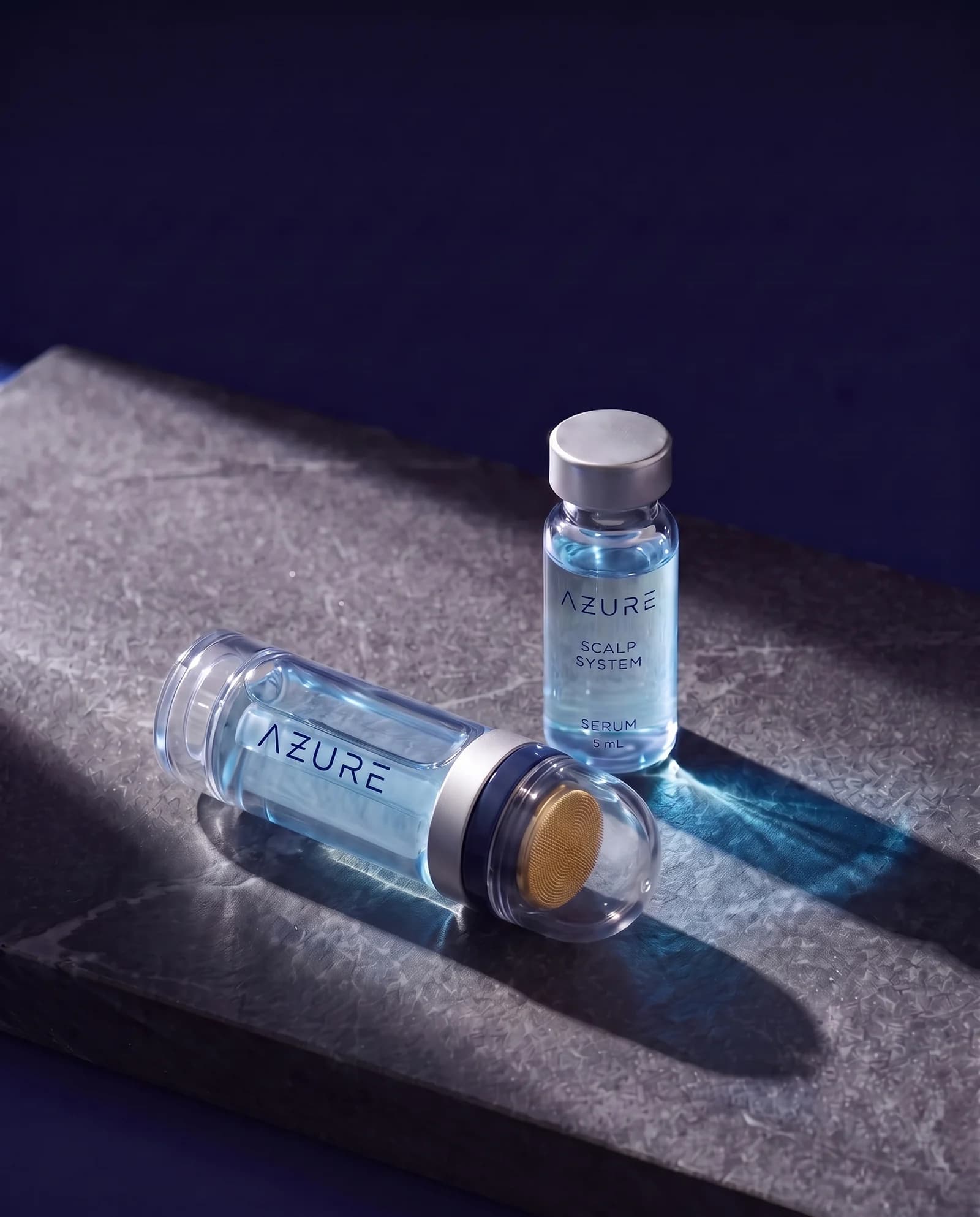 The AZURE applicator lying on dark stone beside a vial of blue serum, in raking light
